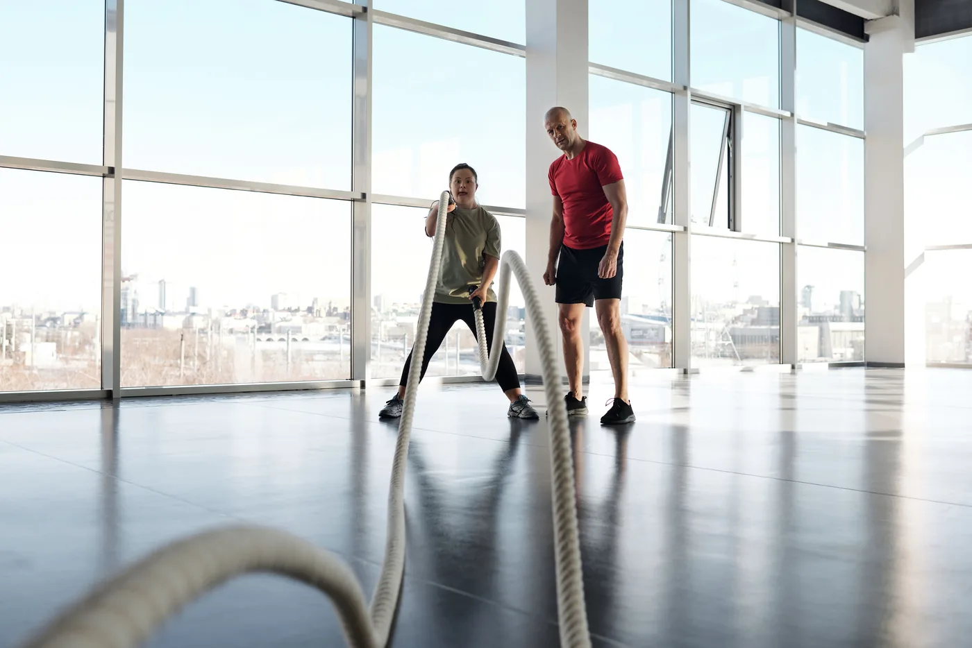 Entrenador supervisando una sesión individual con cuerdas de entrenamiento en un gimnasio.